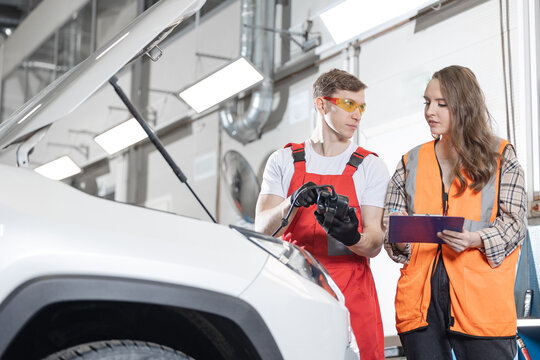 Auto mechanics using diagnostic tool for control battery lvl of car, woman client signs documents of maintenance in garage