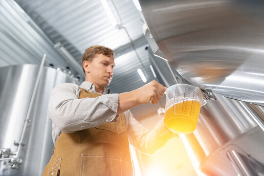 Young caucasian male brewer measuring beer sample in modern brewery. Concept drink industry with Quality control product