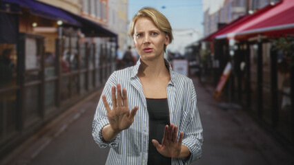 Woman in a striped shirt gesturing with open hands toward camera on a bustling street with sidewalk...