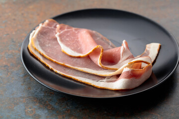 Smoked pork bacon slices on a black plate.