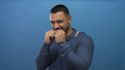 Man in blue polo shirt throwing a punch while winking with clenched fists in a studio setting; determination.