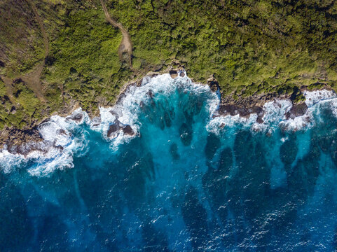 Aerial view of the coastline where the dark green forest meets the turquoise sea and white waves, Guam, United States.