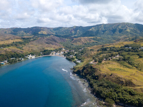 Aerial view of the deep blue bay meeting the shore under the watchful gaze of rugged mountains, a tranquil scene unfolds, Tamuning, Guam.
