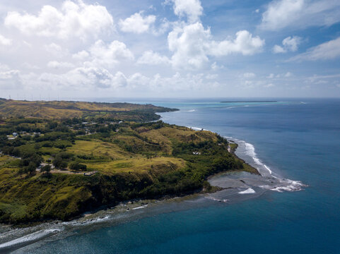 Aerial view of the coastline where the lush green vegetation meets the turquoise sea under the scattered clouds, Guam, United States.