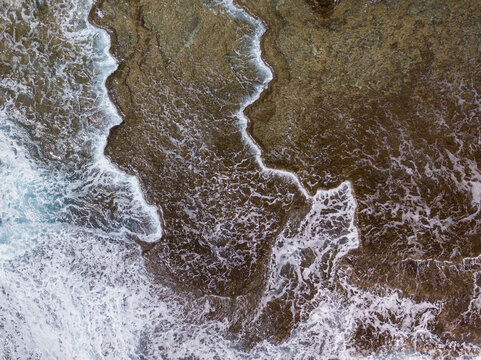Aerial view of the rugged coastline where the sea's foamy embrace meets the textured earth, creating a stark contrast of colors and forms, Guam, United States.