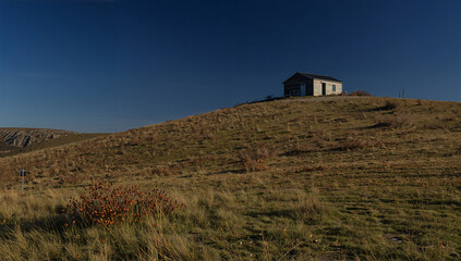 快晴の秋、澄んだ青空の下でオリーブ色の丘と黒い小屋を静かに切り取る