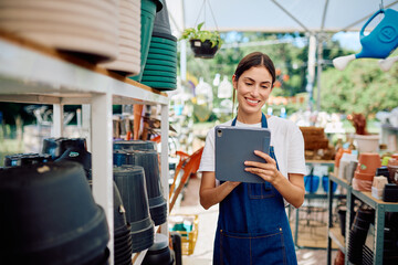 Young woman smiling, wearing an apron, using a digital tablet to manage inventory at her plant...