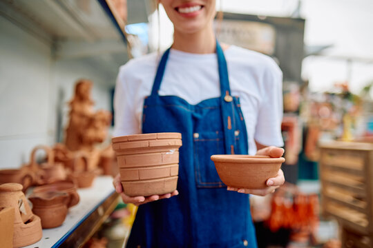 Woman artisan wearing an apron presenting two unglazed terracotta pots, offering traditional handmade ceramics at an outdoor market stall