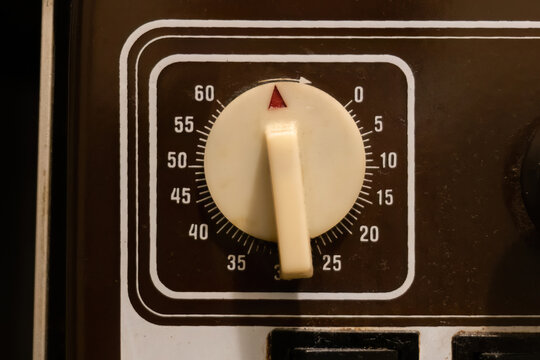Old vintage mechanical 60 minute timer dial with cream turn knob and red pointer on black appliance control panel, closeup front view of analog countdown time selector for oven or microwave