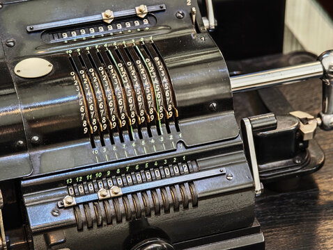 Vintage mechanical calculator and adding machine closeup, black metal counting device with numbered input levers and register wheels, retro office accounting tool, mechanical computing concept