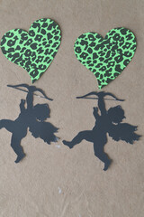 black paper silhouettes of cherubs with bow and two funky green hearts on brown