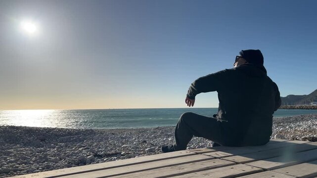 Hombre 50+ descansando en la playa y lanzando piedras al agua