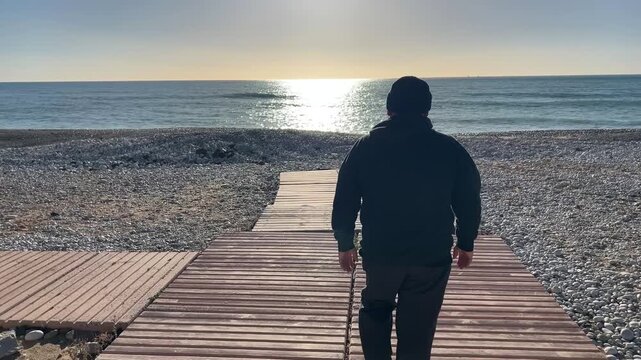 Hombre 50 a&ntilde;os caminando hacia la orilla con c&aacute;mara en seguimiento trasero