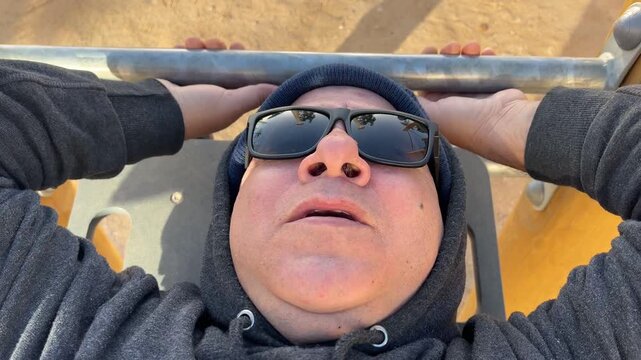 Primer plano de hombre 50+ mostrando esfuerzo en m&aacute;quina de ejercicios al aire libre
