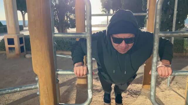 Hombre 50+ realizando flexiones en m&aacute;quina de ejercicios al aire libre