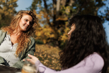 Fototapeta premium Two friends enjoying a sunny day outdoors surrounded by autumn leaves while sharing stories and laughter in a park setting