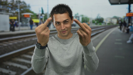 Naklejka premium Young hispanic man flips both middle fingers directly at camera in a busy train station; anger defiance.