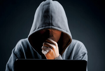 a hacker in hoodie thinking something in front of laptop on dark background