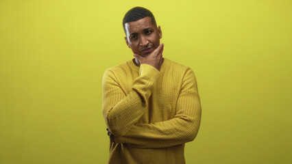 Obraz premium Young black man hand on chin in yellow sweater thinking pose in studio; introspection contemplation calm.