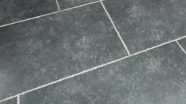 Cleaning grout lines in gray tile flooring at home during afternoon