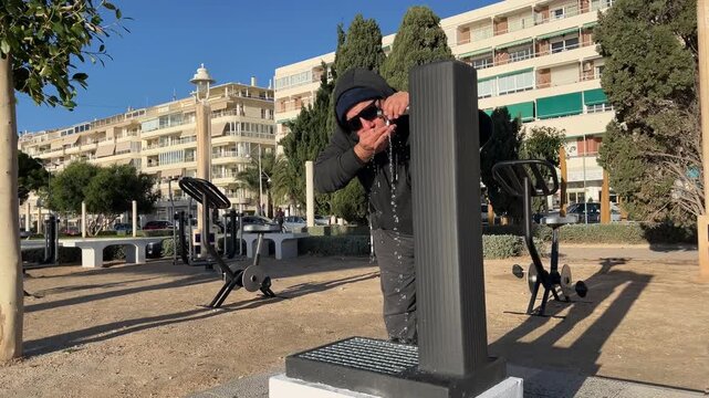 Hombre 50+ hidrat&aacute;ndose en fuente del parque de entrenamiento al aire libre
