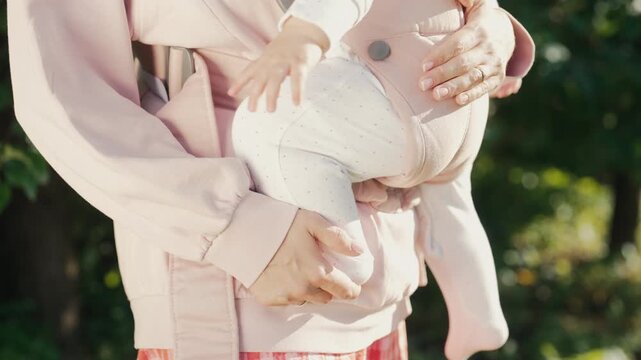 Unrecognizable Mother Holding Baby in Ergonomic Carrier Outdoors. Parenting, bonding, babywearing, care and family lifestyle concepts.