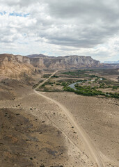 Aerial view of the Chubut River by steppe valley with rock formations and gravel road. Patagonia, Argentina