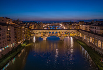 Obraz premium Iconic Ponte Vecchio bridge illuminated at blue hour with reflections on the Arno River in Florence, Italy. Historic architecture and evening city lights create a classic European cityscape