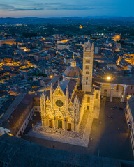 Obraz premium Aerial view of Siena Cathedral (Duomo di Siena) illuminated at blue hour, showcasing Gothic architecture and historic landmarks in the medieval city of Siena, Tuscany, Italy