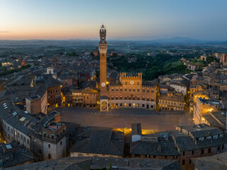 Obraz premium Aerial night view of Torre del Mangia rising above Piazza del Campo in Siena, Tuscany. Illuminated medieval tower and historic city center seen from above during evening hours