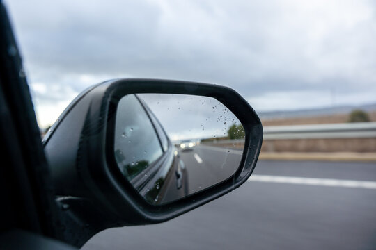 A car's rear view mirror shows a blurry reflection of a car in the distance