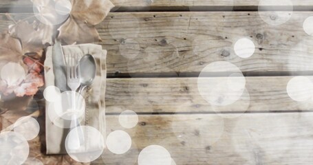 Displaying folded beige napkin holding steel fork and spoon on planks with dried leaves, copy space