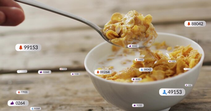 Lifting metal spoon, white bowl holding cornflakes and milk on wood table with notification badges