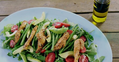 Displaying white oval plate with grilled chicken avocado tomatoes olive oil bottle on rustic table