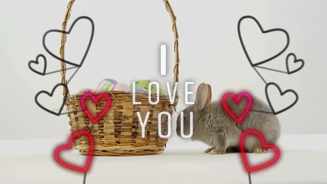 Heart overlays appearing, gray rabbit leaning, sniffing, nudging basket, seeking pastel eggs