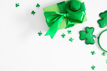 St. Patrick's Day celebration: Green gift box with silk ribbon, leprechaun hat, and shamrock confetti on white background. Minimalist flat lay with copy space for Irish holiday greeting.