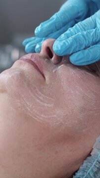 Cosmetology treatment - cosmetologist massaging and cleaning with soap the face of her female client