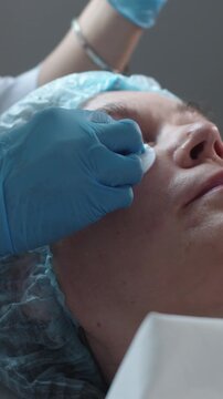 Cosmetology treatment - cosmetologist wipes the client's cheekbones with a cotton pad