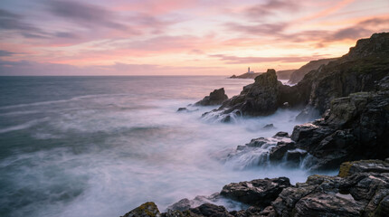 Obraz premium Rocky coast ocean waves dramatic sky sunset lighthouse rugged cliff seascape tranquil scenic nature landscape. scene evokes peaceful and awe inspiring feeling