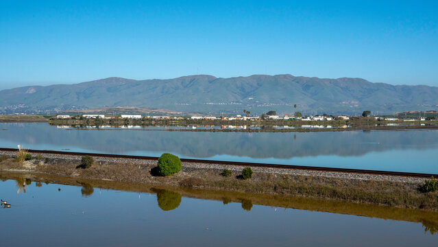 Reflections of Industry: A Californian Landscape with Power Lines, Train Tracks, and Distant Hills Along the Serene Bay Waters