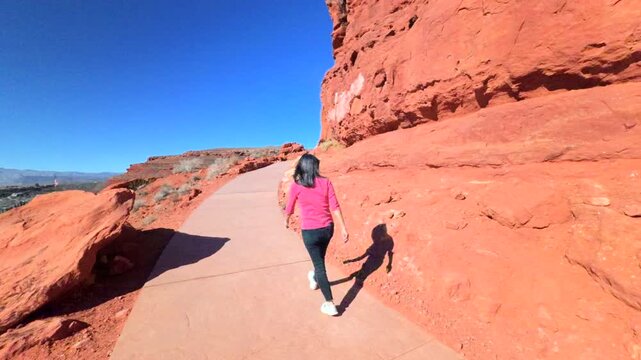 Woman on walking on exploration trail near vibrant red boulders of unique formation sandstone with deep blue sky
