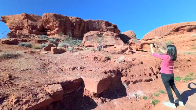 Woman on vacation standing on vibrant red rugged terrain taking photos of rock formation of red sandstone in panoramic shot 60FPS 4k