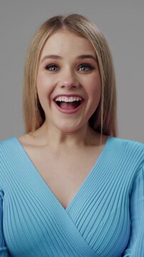 Excited woman smiles widely and claps hands, showing joy in a simple studio setting.