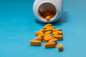 a white plastic bottle lying on its side, spilling orange oval-shaped pills across a textured blue surface.