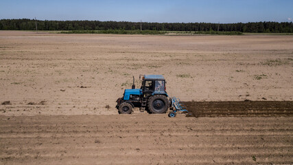 Obraz premium tractor - aerial view of a tractor at work - cultivating a field in spring with blue sky - agricultural machinery