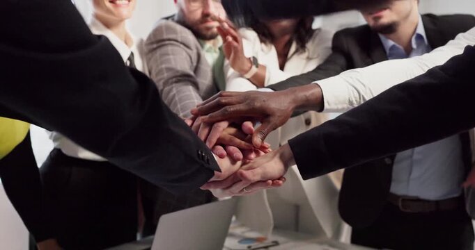 Businesspeople team stack hands in office huddle. Joined palms show support, trust, and commitment at a workplace table during a meeting for success. Clear concept of unity and teamwork.