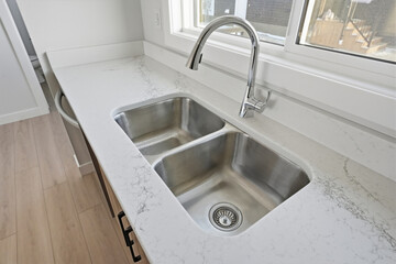 Stainless steel sink with a silver faucet sits on a white marble countertop