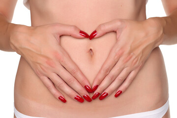 Close-up of a woman forming a heart shape with her hands on her belly around the navel, studio shot...