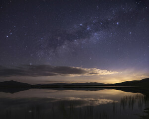 Obraz premium Night sky full of stars reflected on a calm lake with distant mountains Milky Way galaxy