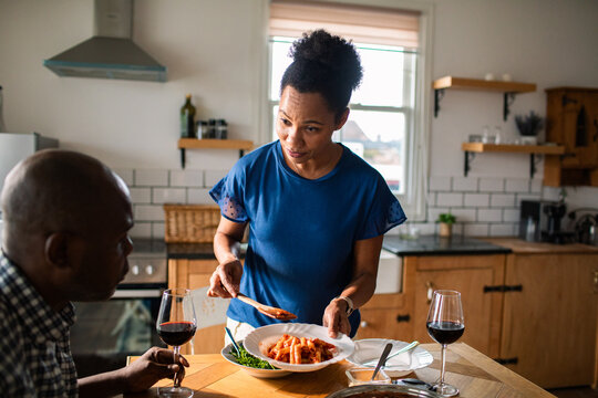 Woman serving pasta to partner in cozy home kitchen